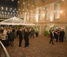 Guests in formal attire mingle under string lights on a brick patio at a Louisiana wedding, showcasing elegant inspiration.