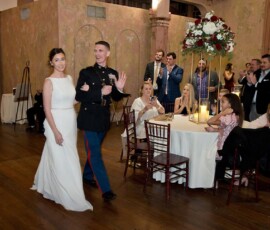 A joyful bride and groom enter their Louisiana wedding reception as guests at round tables watch and applaud.