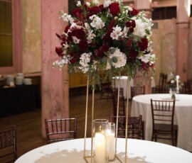 Elegant gold centerpiece with red and white flowers, candles, pink walls, and wooden chairs—Louisiana wedding inspiration.