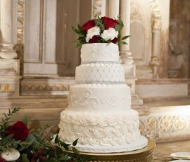 Three-tier white wedding cake with red and white flowers on a gold stand in an elegant, classic New Orleans setting.