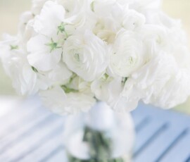 White ranunculus in a glass vase on a dark blue table, offering elegant Gulf South wedding inspiration.