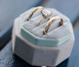 Gold rings, one with a rectangular diamond, in a blue octagonal velvet box on a dark blue wooden surface.