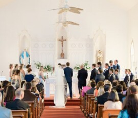 Bride and groom at altar in a Louisiana church wedding, with their party, guests in pews, and statues in the background.