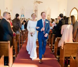 Bride and groom joyfully walk down church aisle as guests clap and celebrate their marriage, capturing true wedding inspiration.