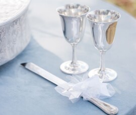 Silver goblets, a white-ribboned knife, and an engraved tray on light blue tablecloth for an elegant New Orleans wedding.