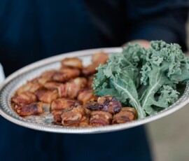 Silver tray with bacon-wrapped appetizers and curly kale, held by someone in dark attire—chic New Orleans wedding inspiration.