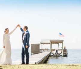 Bride and groom dancing on grass by a dock, with small building and American flag in the background at a Louisiana wedding.