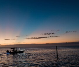 Silhouetted boat glides at sunset on calm water, colorful sky evokes romantic New Orleans-style wedding inspiration.