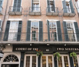 Court of the Two Sisters restaurant in a brick building with green shutters, balconies, plants, and address 613 above the door.