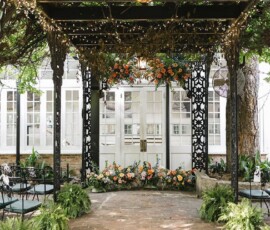 Elegant Gulf South outdoor wedding venue with iron gazebo, string lights, green chairs, florals, ferns, and lush greenery.