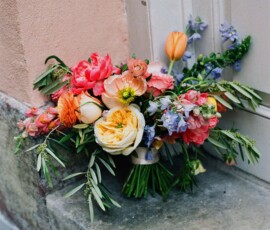 Bouquet of orange, yellow, pink, and purple flowers with green leaves on stone step by white door and peach wall at a Louisiana wedding.
