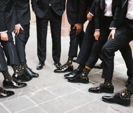 Men in black suits at a Louisiana wedding show off matching patterned socks; only their legs and feet are visible.