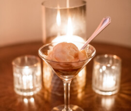 Martini glass with ice cream on a wooden table, surrounded by three lit candles for a warm, cozy vibe.