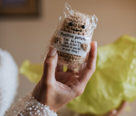 Hand holding a crocheted Positive Potato in clear wrapping with a motivational message, blurred background.