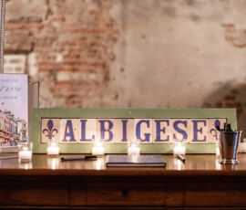 Wooden table with ALBIGESE sign, candles, pens, and a framed guestbook request for Gaby and Andrew.