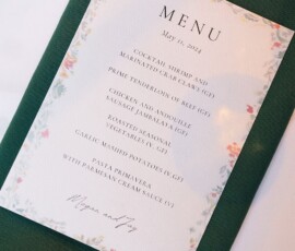 A floral menu with shrimp, beef, chicken, potatoes, veggies, and pasta sits on a green napkin at a Louisiana wedding.