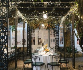 Chic outdoor patio with round tables, white linens, black chairs, string lights, and greenery—ideal for intimate weddings.