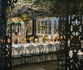 Elegant outdoor dining with black chairs, floral tables, string lights, greenery, and large-windowed building—romantic Louisiana wedding.