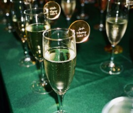 Champagne glasses with nametags on a green tablecloth, filled with sparkling wine—elegant Gulf South wedding inspiration.