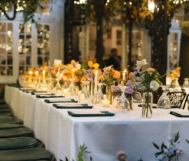 Outdoor dinner table with white linens, flowers, green napkins, candles, and string lights under a vine pergola for a New Orleans wedding.