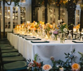Outdoor New Orleans wedding with a long white-tablecloth table, floral centerpieces, candles, and string lights.