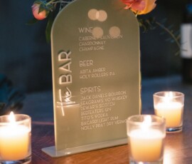 Bar menu with wine, beer, and spirits on a wooden table with candles and flowers at a New Orleans wedding reception.