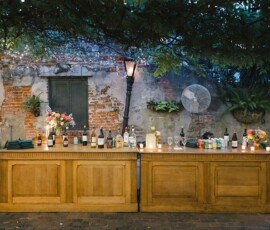Rustic outdoor bar with wood counters, drinks, flowers, string lights, and cozy evening vibes for a Louisiana wedding.