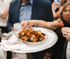 A person serves skewered cherry tomatoes and cheese at a lively Louisiana wedding as guests eagerly reach for the platter.