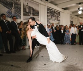 Bride and groom share a romantic dance dip on a checkered floor as smiling guests in formal attire watch at their elegant reception.