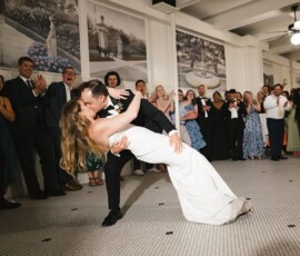 Bride and groom dip and kiss on the dance floor as guests cheer, with Louisiana-inspired wall murals in the background.