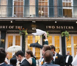 Crowd celebrates outside Court of the Two Sisters in New Orleans, waving napkins and umbrellas at a lively wedding reception.