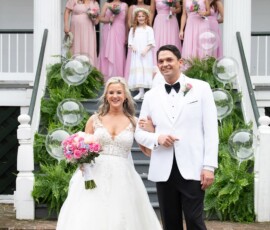 Bride and groom smile on steps with bridesmaids in pink; bubbles, greenery, and florals create romantic wedding inspiration.