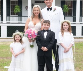 Bride, groom, and three kids smile outside a white columned house in classic Louisiana wedding attire.