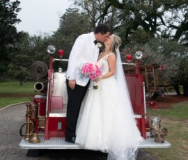 Bride and groom kiss on a vintage red fire truck, surrounded by greenery at their Louisiana wedding.