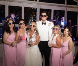 Bride and groom in heart sunglasses pose with five bridesmaids at a lively New Orleans wedding with live band.
