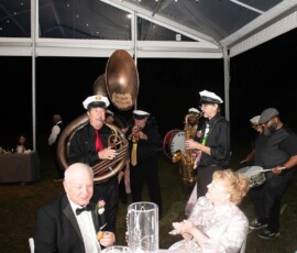 Brass band in sailor hats plays under clear tent at night during a Gulf South wedding, guests in formal attire enjoying the lively scene.