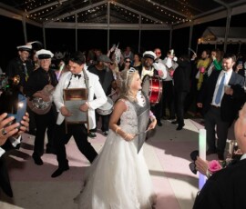 Bride and groom play washboards at a lively New Orleans wedding with brass band and guests under string-lit tent.