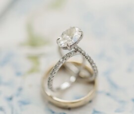 Diamond engagement ring and gold wedding band on a blue-green floral surface, elegant Gulf South wedding style.