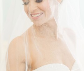 Bride in a white strapless dress and veil smiles, looking down during her Gulf South wedding in soft lighting.