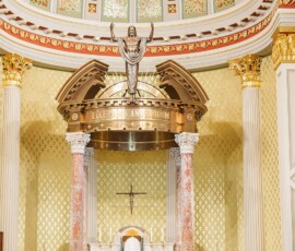 Bride and groom at the altar of a grand New Orleans church with gold accents, tall columns, and attendants on both sides.