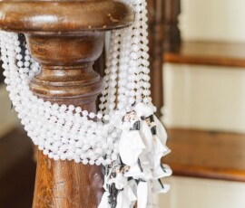 White bead garlands and bride and groom figurines decorate a wooden stair banister, perfect for classic Gulf South weddings.