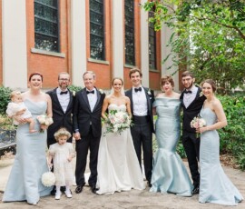 Bride and groom at center of outdoor Louisiana wedding, smiling with family, friends, and two children in formal attire.
