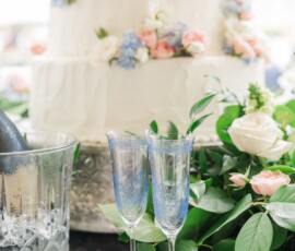 Empty champagne flutes and floral decor sit before a white cake with pink and blue flowers at an elegant Louisiana wedding.
