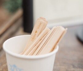 White cup with blue monogram holding engraved wooden ice cream sticks on a wooden surface, ideal for a Louisiana wedding.