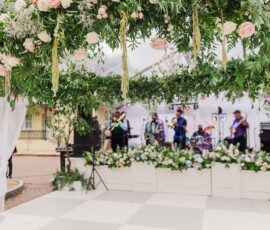 Flower arch above white dance floor and live band onstage create stunning Louisiana wedding reception scene.