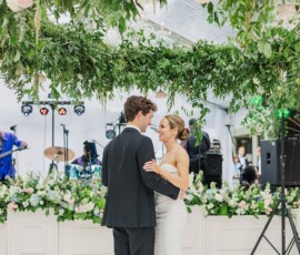 Bride and groom share their first dance under a floral arch with pink roses at a Louisiana wedding, live band behind them.
