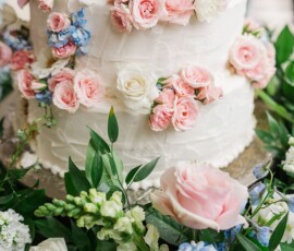 White tiered cake with textured icing, pink roses, blue hydrangeas, and greenery—ideal for New Orleans or Louisiana weddings.