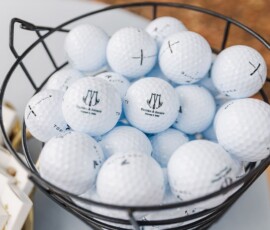 Black wire basket of logo-marked white golf balls, some with hand-drawn Xs, adds playful New Orleans wedding decor.