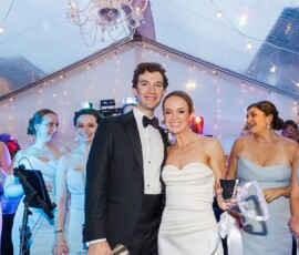 Bride and groom smile with bridesmaids in light blue under a clear tent at a joyful Louisiana wedding reception.