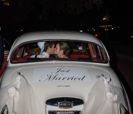 Couple kissing in a vintage white car with Just Married sign and tulle, seen from behind at night—romantic Louisiana wedding.